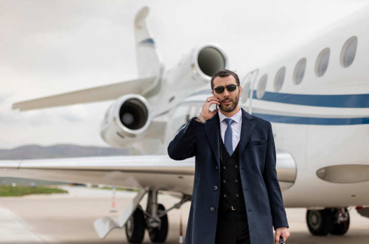 Business executive standing beside a private jet, highlighting the need for executive close protection and enhanced security measures during international corporate travel. 