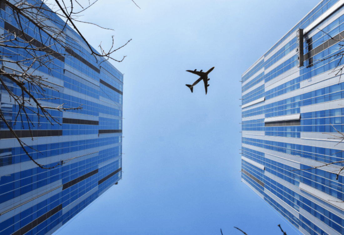 Airplane flying between modern city skyscrapers, symbolising international travel exposure and the importance of travel risk management and protective security planning.